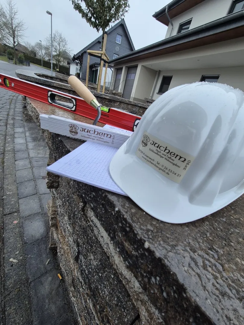 Wasserwaage, Meterstab und Bauhelm der Firma Juchem auf einer Mauer